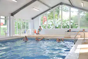 Innenpool im Campinghaus mit Kindern im Wasser, Glasfront und Liegen am Beckenrand.