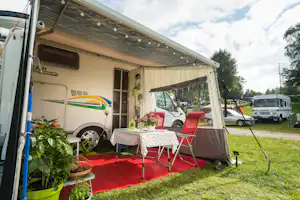 Wohnwagen mit Vorzelt, rotem Boden und Tisch mit Stühlen auf dem Stellplatz, daneben geparkte Autos und Wohnmobile.