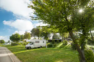 Wohnmobil auf einem Campingplatz am Grasweg, neben Hecken und Bäumen, im Hintergrund weitere Fahrzeuge.