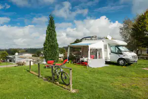 Wohnmobil mit Vorzelt und Terrasse auf einer grünen Campingwiese, daneben ein Fahrradständer und weitere Stellplätze.