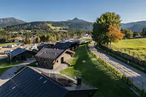 Campinganlage mit mehreren Ferienhäusern und Solardächern, gepflasterten Wegen und Rasenflächen, im Tal mit Bergen im Hintergrund.