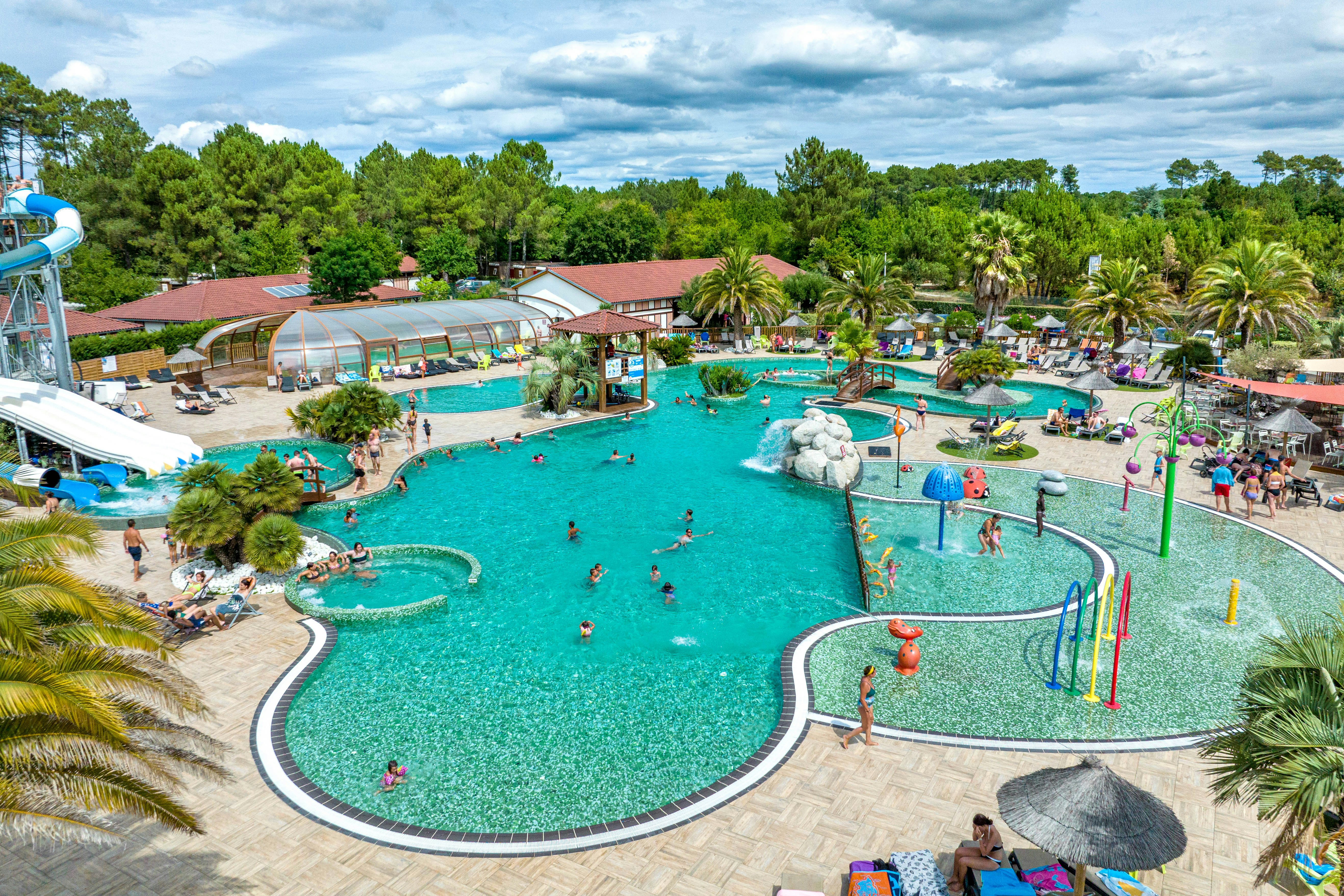 Camping Au Lac de Biscarrosse - Ciela Village - Poollandschaft mit Wasserrutschen umgeben von Palmen