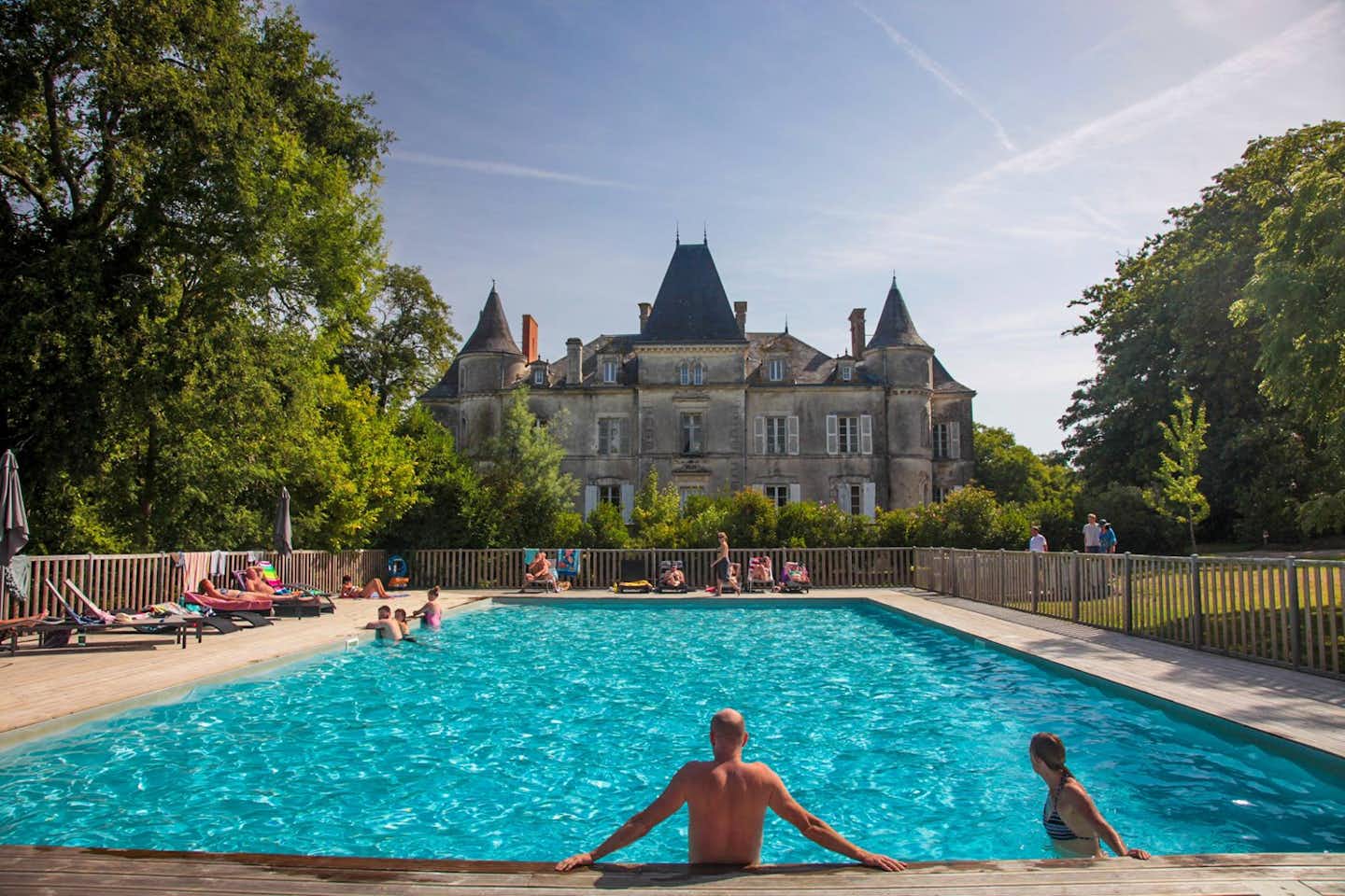 Yelloh! Village Château de la Forêt - Poolbereich mit Liegestühlen mit Blick auf Schloss auf dem Campingplatz