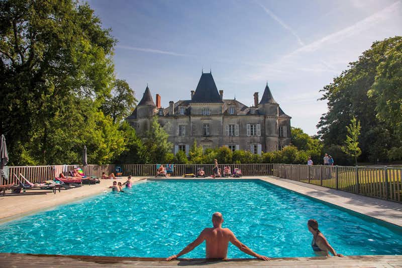 Yelloh! Village Château de la Forêt - Poolbereich mit Liegestühlen mit Blick auf Schloss auf dem Campingplatz