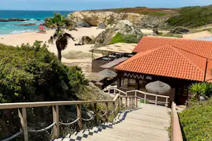 Terrasse mit Geländer und Sitzbereich am Campinghaus mit rotem Ziegeldach, Blick auf das Meer und den Strand in der Ferne.