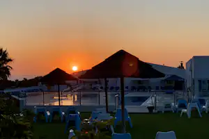 Campinganlage mit Pool und Liegestühlen, Blick auf die Dächer der Unterkünfte bei Sonnenuntergang.