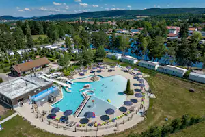 Luftaufnahme eines Campingplatzes mit großem Schwimmbecken, Liegen am Rand, Wegen und Bäumen in der Umgebung.
