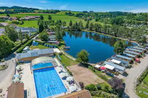 Luftaufnahme eines Campingplatzes mit großem Pool, Liegen am Beckenrand, Wohnmobilen und kleinen Gebäuden am Seeufer.