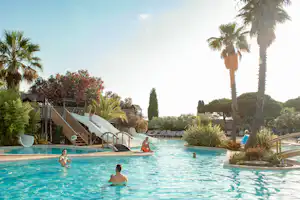 Großer Camping-Pool mit Palmen, Sonnenliegen und Treppe, im Hintergrund Bungalows und Pflanzen im Garten.