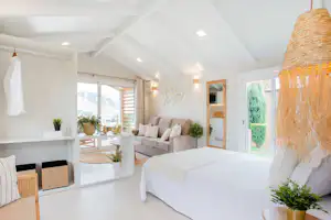 Wohnbereich mit Bett und Sofa in einem hellen Zelt- oder Wohnwagenraum, große Fenster und Deko-Pflanzen im Innenraum.