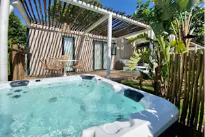 Whirlpool im Garten mit Pergola, Liegen und Sichtschutzzaun, daneben Pflanzen und ein kleiner Weg.