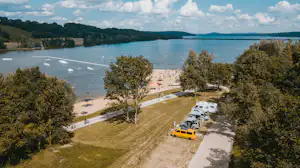Campingplatz am Flussufer mit Stellplätzen für Wohnmobile, Grasfläche, Bäumen und Blick auf das Wasser.