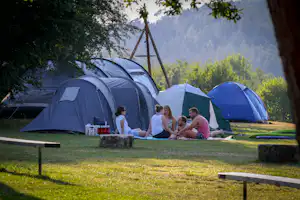 Zeltgruppe auf einem Campingplatz im Grünen, mit Picknicktisch und Sitzbereich vor mehreren Zelten im Hintergrund.
