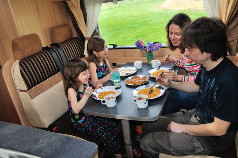 Familie im Wohnmobil am Tisch.
