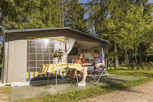 _0001_Camping-Olympia---Camperpaar-vor-ihrem-Wohnwagen-in-der-Sonne.png