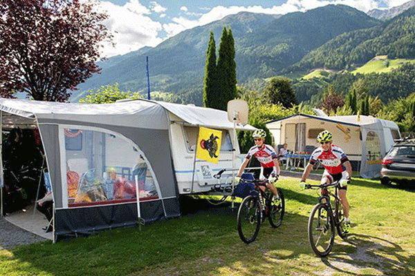 _0000_Camping-Residence-Saegemuehle---Fahrrad-Fahrer-auf-dem-Campingplatz-Gelaende-mit-Blick-auf-die-Berge.png