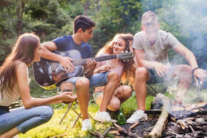 Jugendliche sitzen mit Gitarre am Lagerfeuer