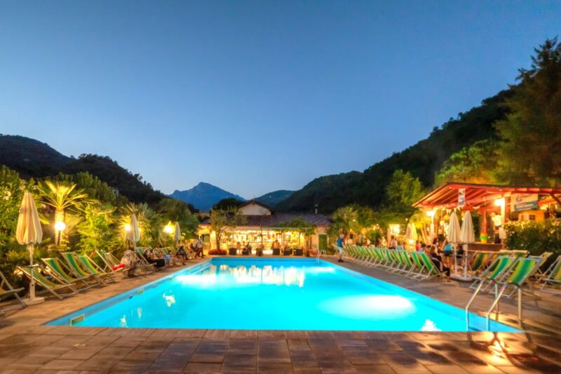 Poolbereich mit Liegestühlen und Beleuchtung am Abend auf dem Campingplatz