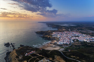 Luftaufnahme des Dorfes Zambujeira do Mar und des Strandes bei Sonnenuntergang, in Alentejo, Portugal