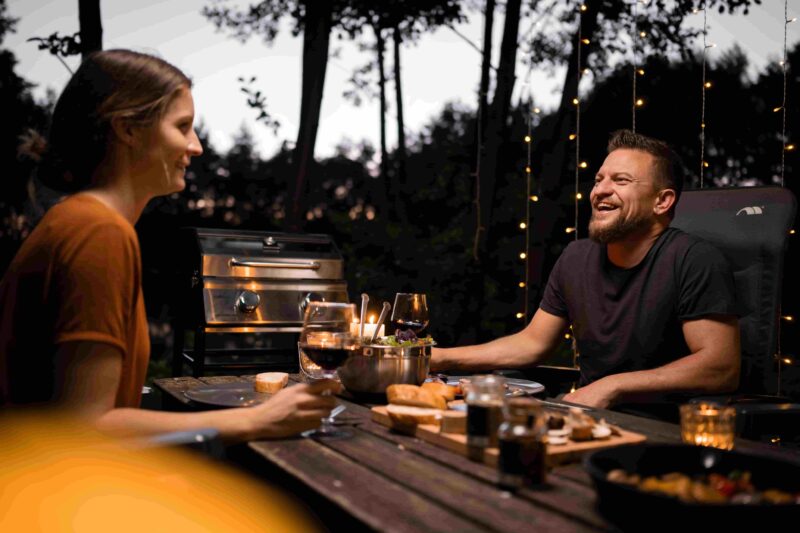 Ein Paar trinkt Wein neben dem Campervan und dem Grill