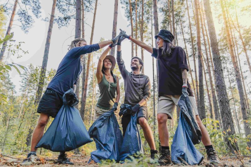 Gruppe von Freiwilligen, die sich um die Natur kümmern und Müll in Plastiktüten sammeln